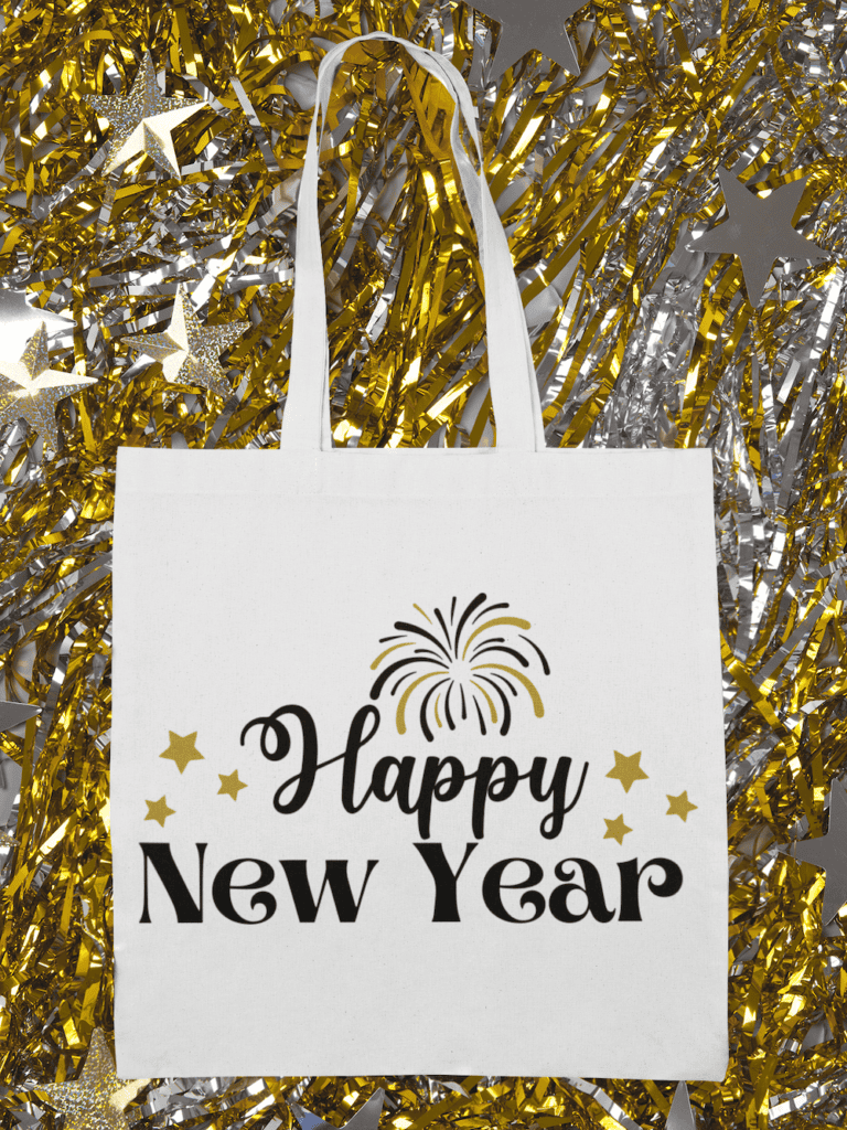 A white tote bag with 'Happy New Year' text in black and gold, featuring a firework design and surrounded by gold and silver tinsel decorations.