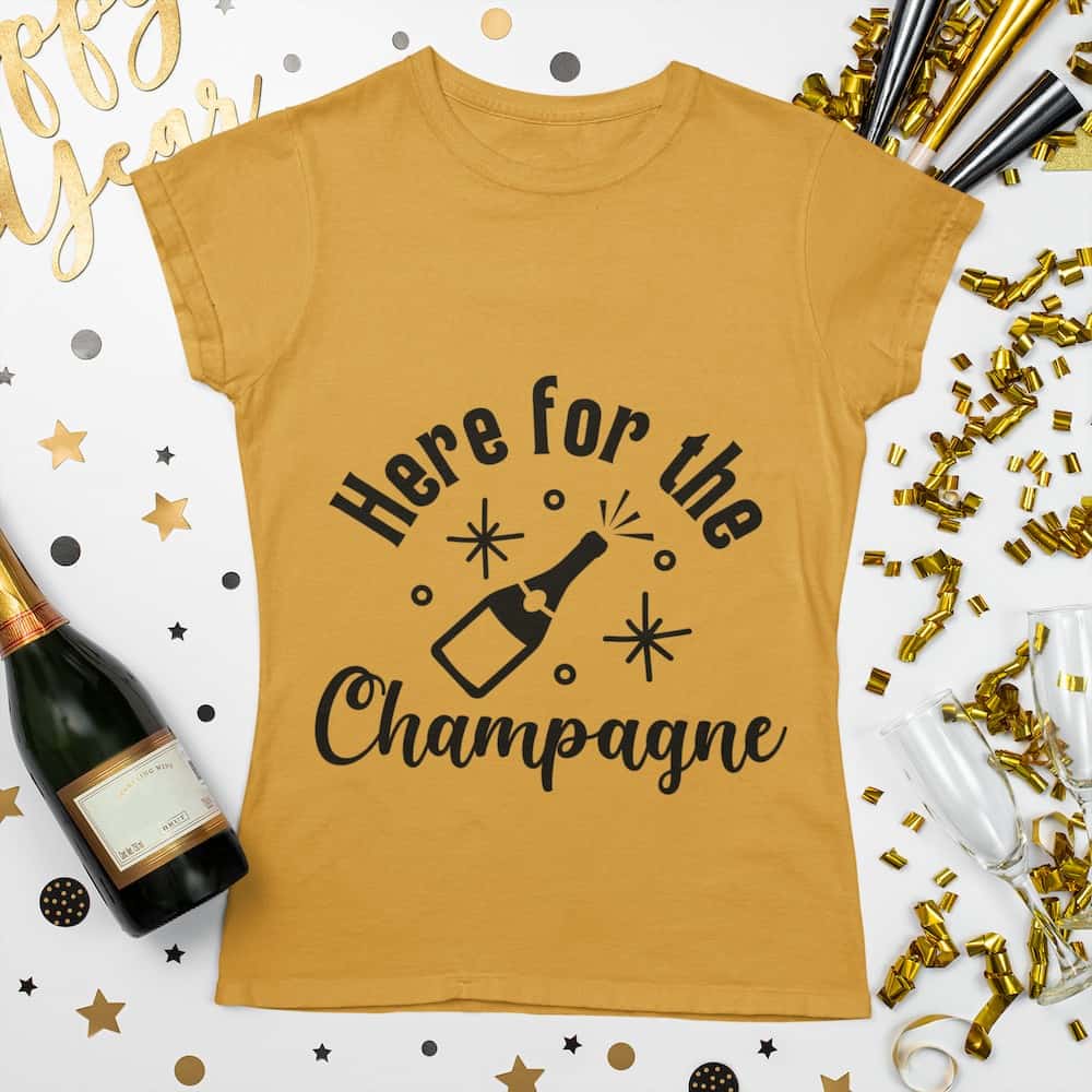 A gold t-shirt with 'Here for the Champagne' text and a champagne bottle design, styled with gold and silver New Year's party accessories.