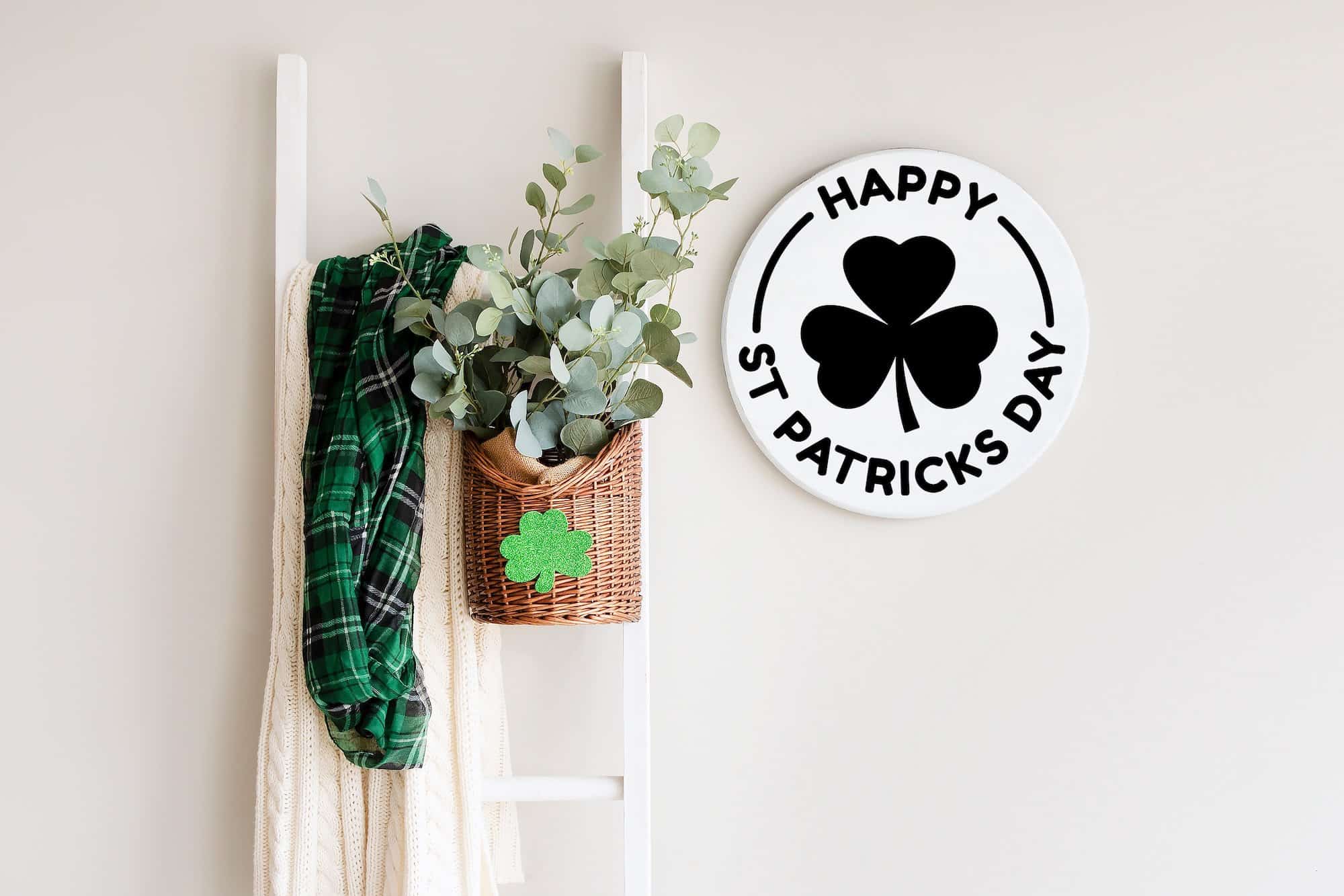 Minimalist round 'Happy St. Patrick’s Day' sign featuring a black shamrock and curved text, styled with a green plaid scarf and rustic décor. 